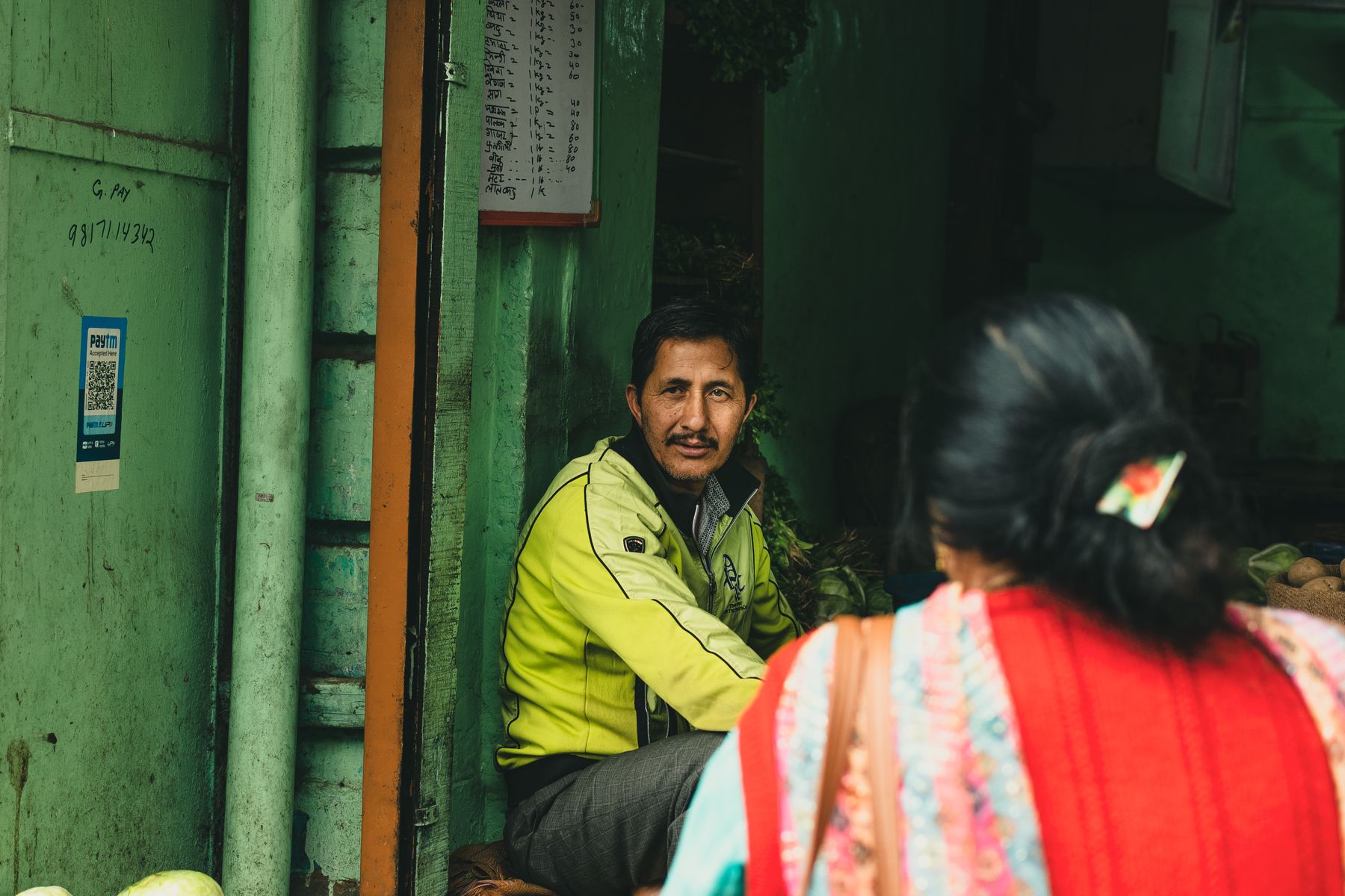 A local market merchant speaking with a customer at the counter